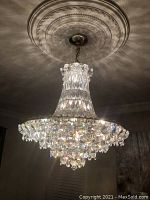 Large crystal chandelier installed on ceiling with decorative ceiling medallion visible, showing overall shape and light dispersion.