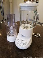 Full view of Cuisinart blender with glass pitcher and food processor attachment beside it on countertop.