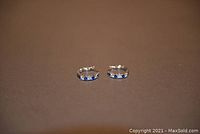 Pair of small silver-tone hoop earrings with blue stones photographed on a dark brown background.