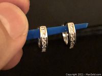 Close-up of the small silver-tone hoop earrings held by a finger illustrating detail and size.