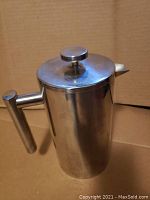 Closed French press showing metallic silver stainless steel cylindrical body and knob lid.