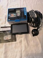 Photo of Garmin Nuvi 2595LM GPS device with accessories including mount, car charger, manuals, and original box set on beige surface.