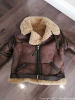 Frontal view of brown sheepskin flying jacket laid flat showing zip front, shearling collar and belt