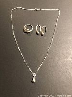 Top-down view of the entire jewellery set on a dark surface, showing necklace, ring, and earrings.