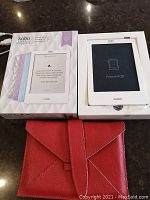 Kobo e-reader in original packaging powered off, with red textured cover shown in foreground