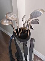 Photo showing golf clubs standing inside the golf bag against a wall, displaying tops of grips and club heads