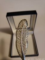 Silver leaf brooch standing upright in black and white jewelry box showing detailed leaf veins and shape.