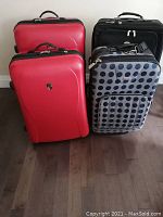 Four suitcases together - two red hard cover Heys luggage, one black Landau soft-sided luggage, and one gray polka dot Travelers Club soft suitcase