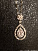 Close-up photo of the necklace pendant showing a teardrop shape with a central pear-shaped stone and surrounding smaller stones on a black background.