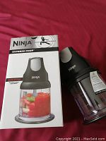 Photo of Ninja Express Chop box and one assembled unit showing chopping container with food inside and motor base upright next to box.