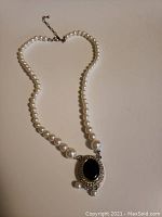 Full view of the pearl necklace with the large black onyx pendant surrounded by small diamonds and three pearl drops hanging from the pendant.