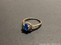 Front angle of silver-tone ring showing blue center stone and clear accent stones.