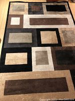 Photo of the full rug laid flat on wooden flooring showing the geometric pattern design and color scheme.