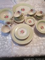 Full set displayed on table showing teacups, saucers, plates, bowls, platter, creamer and sugar bowl with soft green and gold edges and pink rose floral design.
