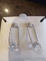 Close-up of the earrings showing the silver chain link drop and clear crystal bead at the bottom.