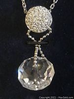 Close-up photo of the crystal pendant showing large faceted crystal with smaller round crystal-studded ball above on silver-tone chain.