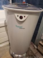 Full view of white cylindrical towel warmer with transparent lid and control panel on front.