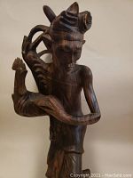 Front view of the carved wooden figurine showing the detailed face, arm holding the animal head, and the extended carving from the back.