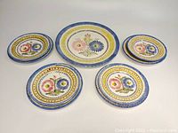 View of entire plate set including one large serving plate, four medium plates, four smaller plates with one broken.