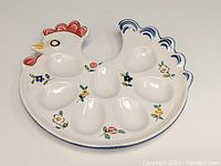 Full top view of ceramic hen-shaped egg serving platter showing 7 egg indentations and floral decorations.
