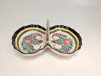 Top view of the divided serving dish showing the two scalloped bowls each decorated with pink and green floral motifs with a black and yellow border and a center handle.