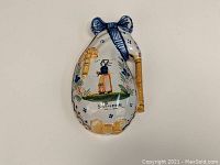 Front view of ceramic wall pocket vase in the form of a bagpipe showing painted Breton woman and decorative bows.