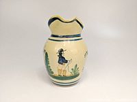 Front view showing the painted Breton man figure below the spout, cream-yellow glaze and some foliage designs.