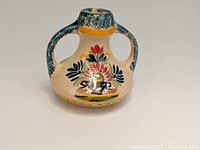 Front side of HenRiot Quimper two-handled vase showing floral decoration on cream background with blue speckled handles and rim.