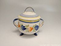 Front angle view of the HenRiot Quimper footed pot sugar bowl with floral decoration on white ceramic body, showing handles and lid.