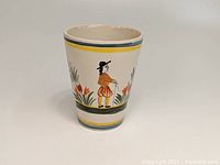 Side view of the ceramic beaker featuring the hand-painted Breton man motif and floral decoration, showing the conical shape and color accents on rim and base.