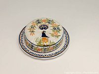 Front angle of covered butter/cheese dish showing the Breton man motif on lid and floral decoration on base plate.