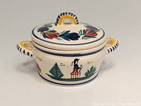 Front view of pottery jar and lid featuring Breton man motif with floral decoration and two handles on jar sides.