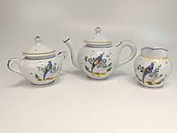 Three-piece HenRiot Quimper pottery tea service set showing teapot, sugar bowl, and creamer with blue bird decoration.