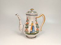 Side view with Breton woman motif in traditional dress, showing the square body, decorated handle, and floral patterns.