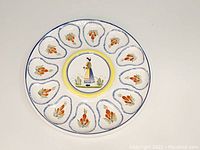 Full view of large white ceramic oyster plate/platter with painted decorations including a Breton woman figure and orange flower motifs in oyster-shaped sections.