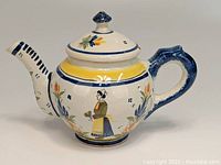 Side view showing the painted Breton woman figure in traditional dress and floral motifs on ceramic teapot.