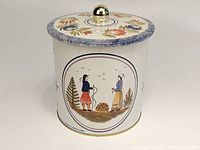Front view of the canister showing the lithographed image of two figures and detailed floral design around the edge of the lid with golden knob.