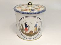 Front and side view of the lithographed tin canister showing a folk art-style scene of a man and woman in traditional attire with floral decorations.