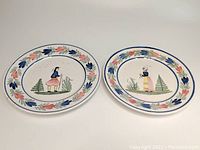 Pair of oval 10 3/4 inch Grande Maison Quimper plates showing hand-painted Breton man on one plate and Breton woman on the other, floral border decoration.