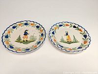 Pair of scalloped edge plates, 7 inch diameter, featuring hand-painted Breton man and woman, showing full front view of both.