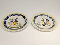 Front view of both 8-inch Henriot Quimper plates with Breton man and woman designs, showing full artwork and rim colors.