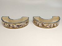 Pair of two curved ring dishes with painted farm animal and floral motifs on cream faience base. Blue diagonal stripe accents the rims.