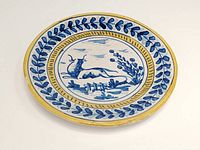 Top-down view of round faience plate showing blue bull motif center with leaf patterned border and yellow rim.