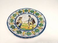 Top-down view of the ceramic plate showing the hand-painted French country scene of two figures and floral decorative border.