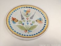 Top down view of round faience stoneware plate with floral painted decoration in multiple colors and a day yellow and blue dot border.