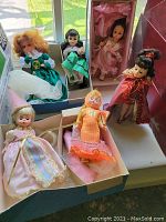 Photo showing six Madame Alexander dolls in various costumes including green, pink, red, and orange dresses, some in original boxes