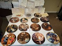 Overview of 15 collector's plates laid out on a table with accompanying certificates and paperwork.