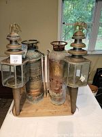 Pair of antique carriage lamps with eagle finials alongside two vintage fire extinguishers displayed on a wooden base in front of a window.