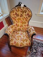 Front view of the carved wooden parlor chair with floral upholstery.
