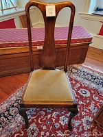 Front view of antique mahogany side chair with upholstered tan seat and carved cabriole legs. Chair is placed on patterned rug and near a wooden bench with red cushion.